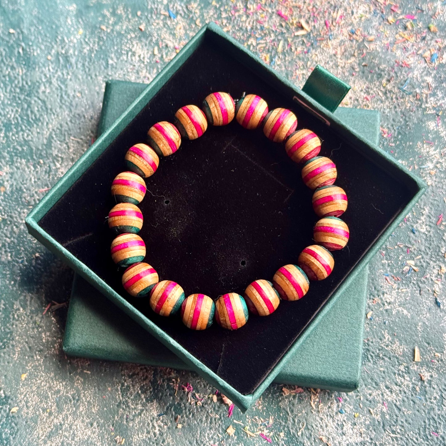 Pink and Teal Skateboard Bracelet made of round beads with alternating pink and teal stripes displayed in a green presentation box.