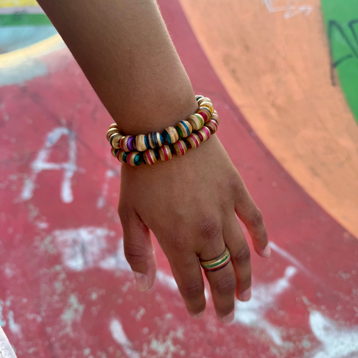 Skateboard wood bead bracelets worn stacked on the wrist against a painted ramp, colours vary by deck.