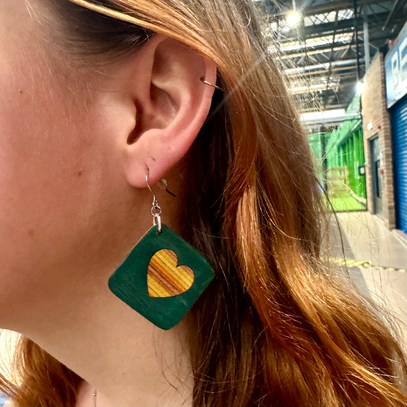 Lightweight recycled skateboard square drop earring shown being worn, with a heart cut-out and layered maple centre.