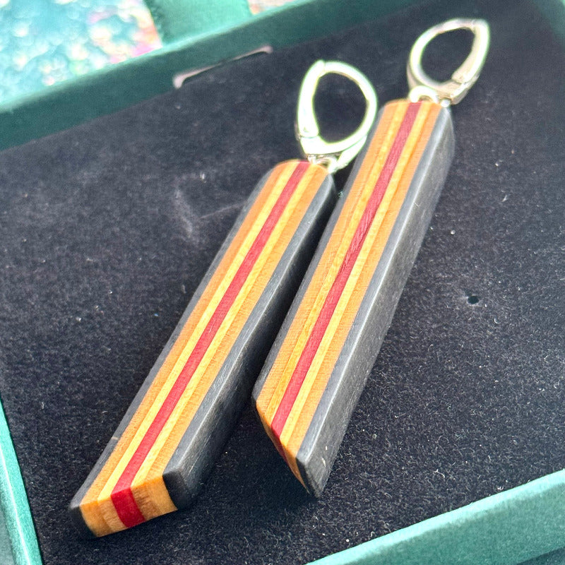 Wooden earrings with red and gold stripes on a dark surface