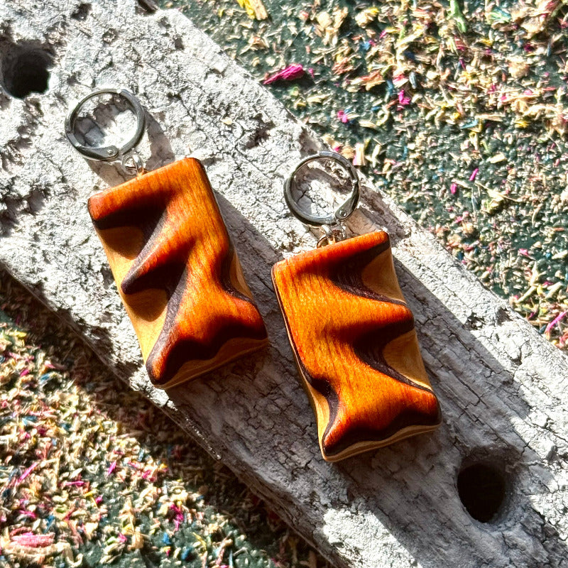 Wooden earrings with a zigzag design on a textured surface