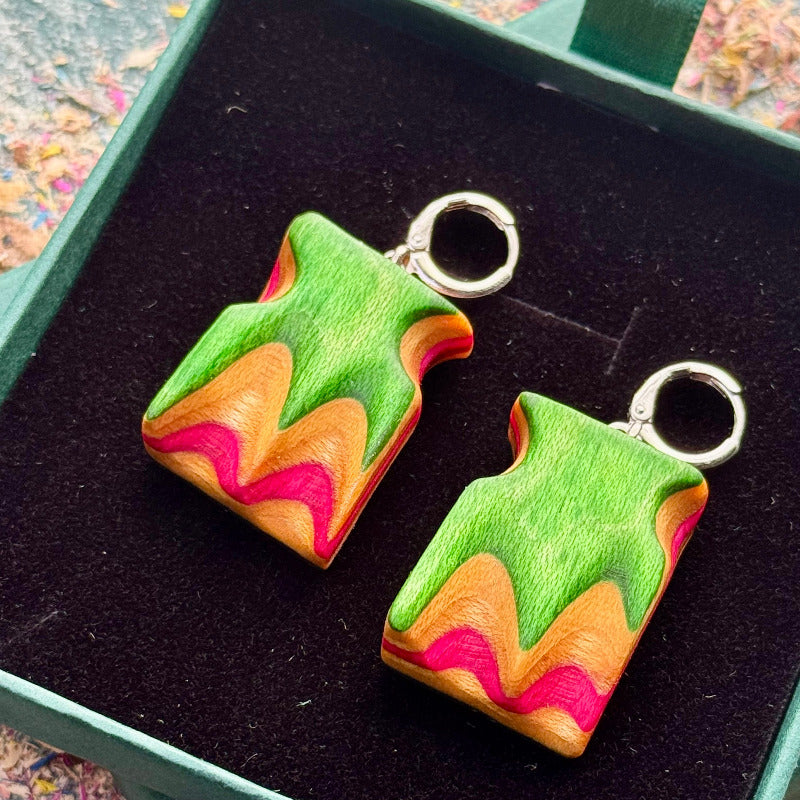 Colorful earrings with green, orange, and pink design on a black background
