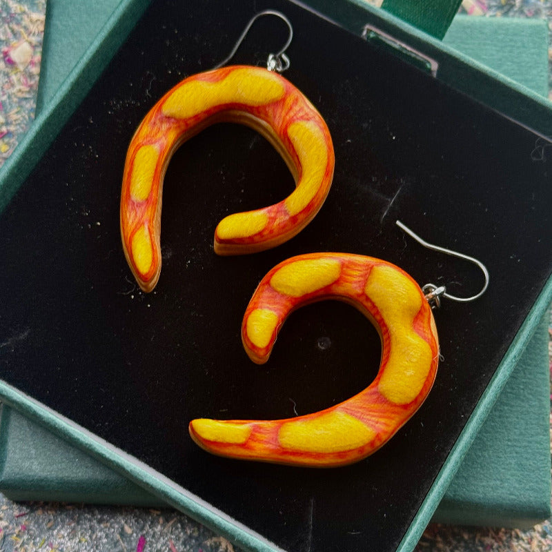 Pair of orange and yellow curved earrings on a black display stand.