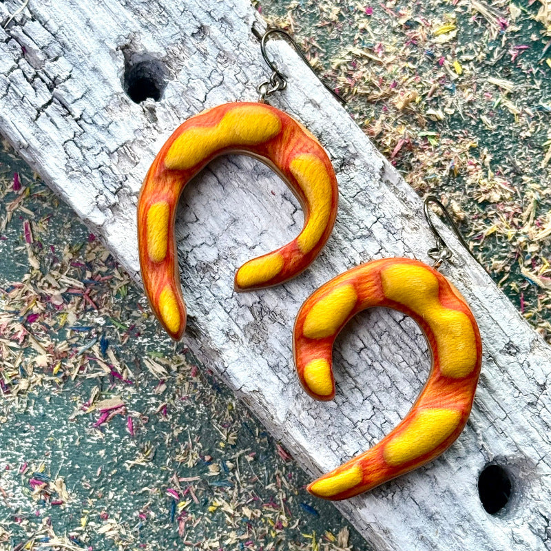 Pair of orange and yellow curved earrings on a textured surface.