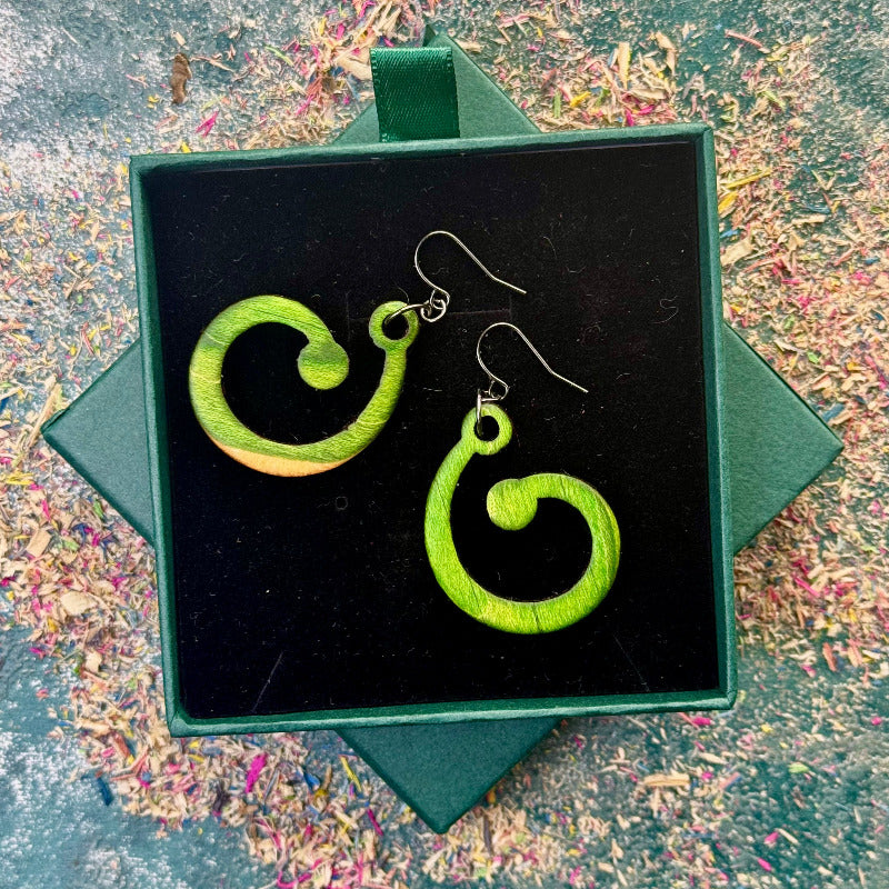 Green spiral earrings in a black box on a textured surface