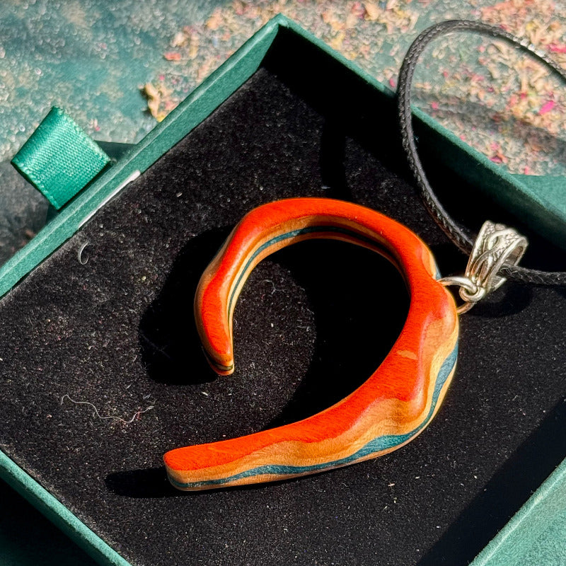 Wooden pendant with a silver chain on a black cushion in a green box.