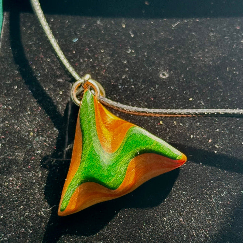 Triangular pendant with green and orange design on a dark surface