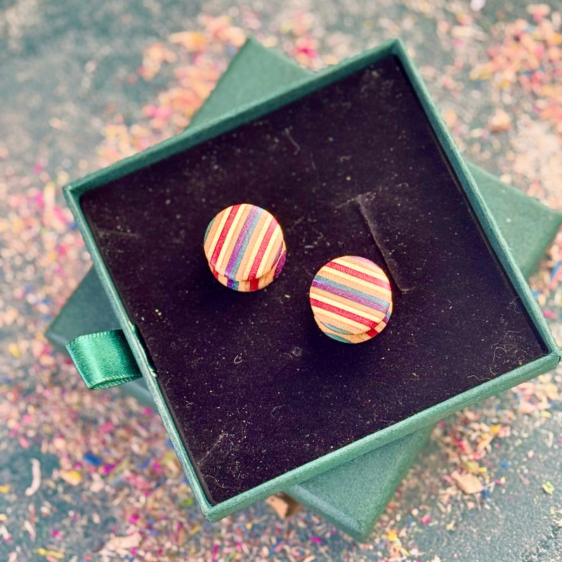 Colourful recycled skateboard wood plugs displayed in a green jewellery box, showing smooth rounded shape and striped colour tones.