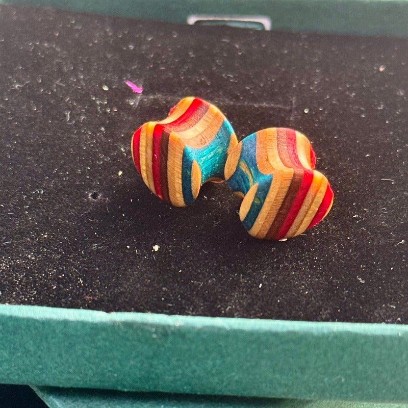 Handmade wooden plugs crafted from recycled skateboard wood with bright blue, red and natural tones, photographed on a dark jewellery box.