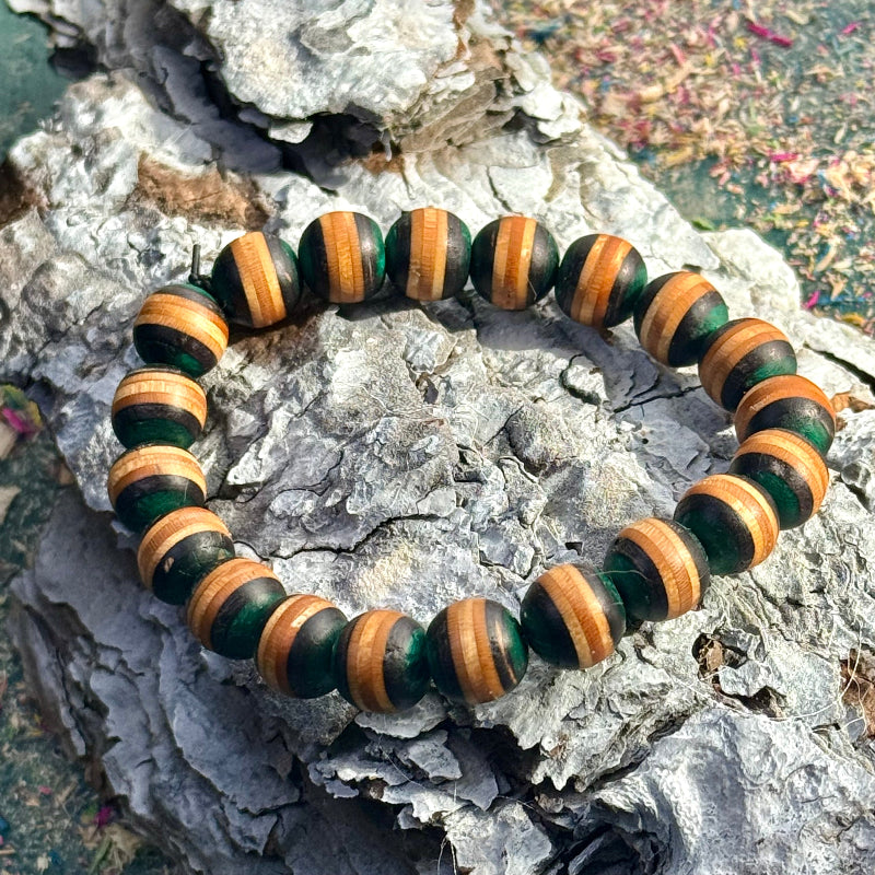 Recycled skateboard wood bracelet with rounded beads showing green colour tones, photographed on textured tree bark.