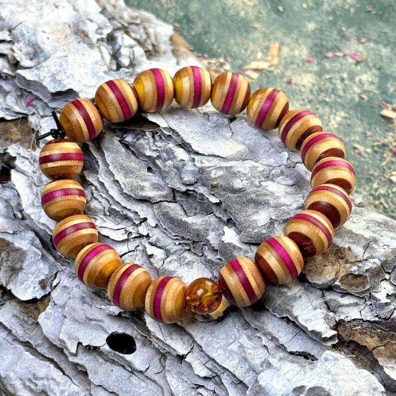 Bracelet made from recycled skateboard wood in yellow, pink and brown colour tones, finished with one amber accent bead and shown resting on textured bark.