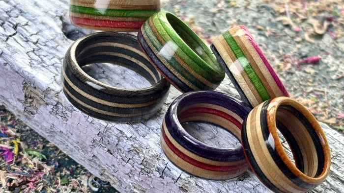 Five recycled skateboard wood rings resting on weathered timber, with green, pink, purple and red layers showing