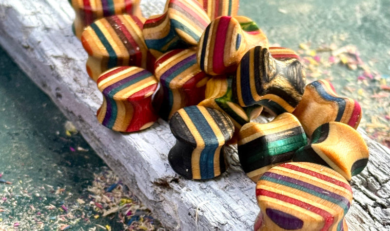 Double flare wooden ear plugs cut from recycled skateboard maple, resting on weathered timber