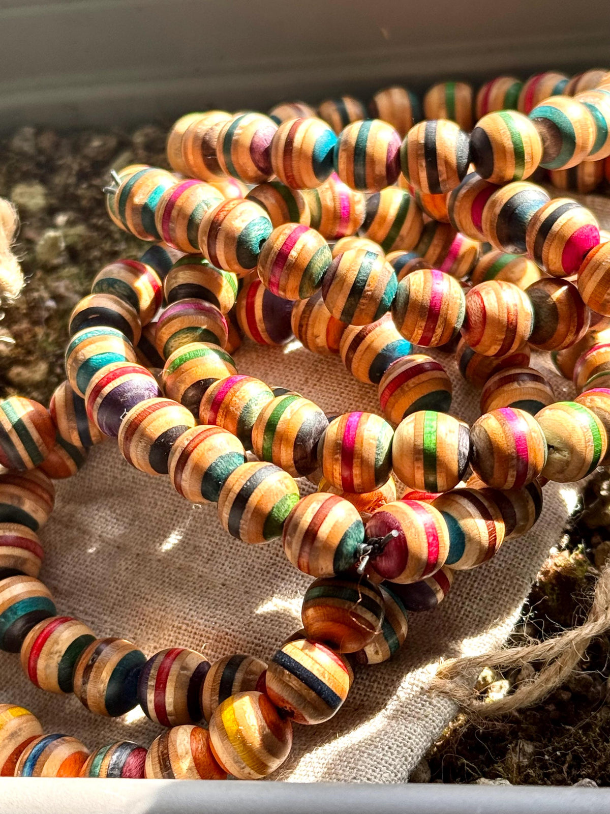 Recycled skateboard wood bead bracelets piled together, showing round beads with pink, teal, green, red and natural maple stripes.