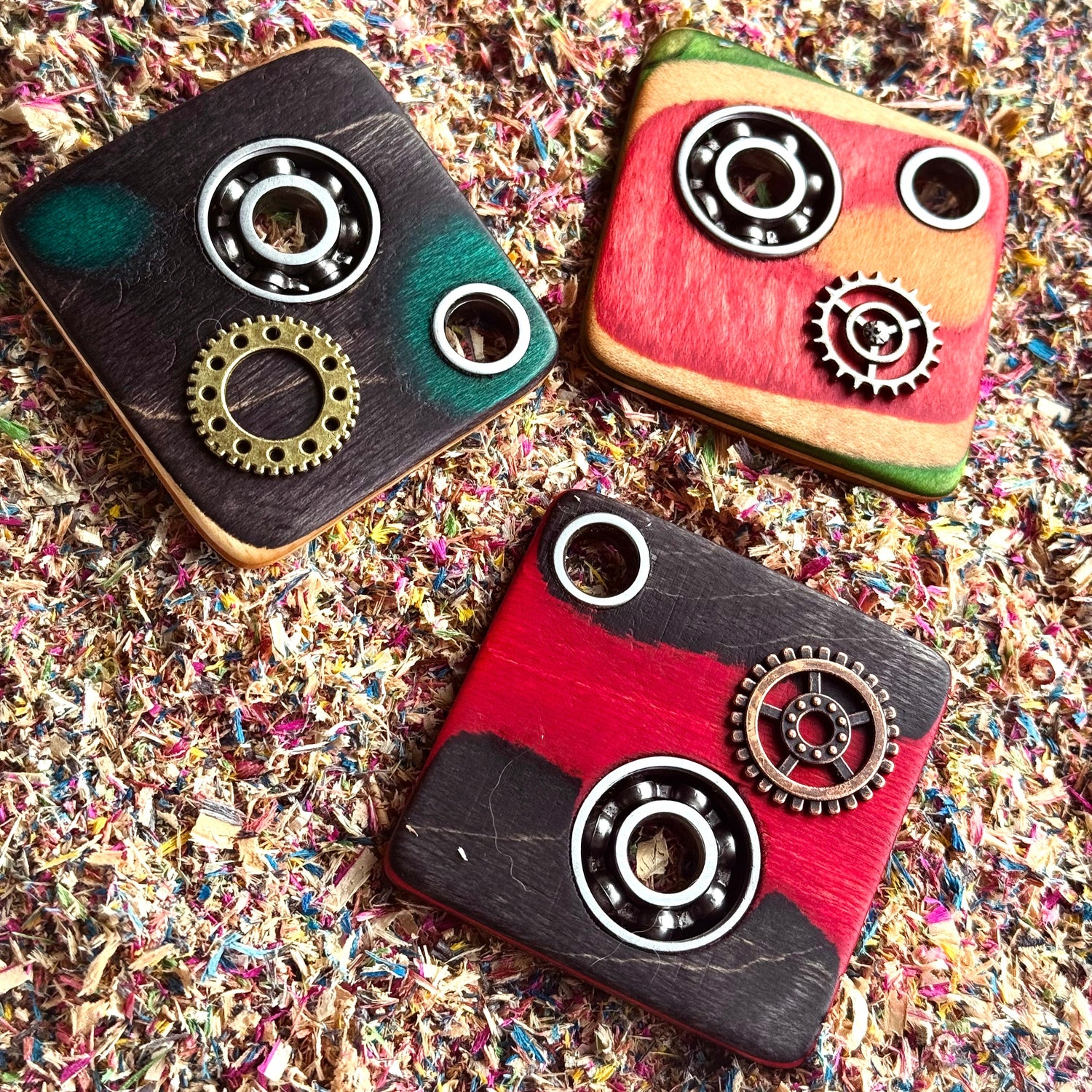 Set of industrial skateboard pendants handmade from recycled decks with ball bearings and gear details, featuring black, red, and green wood layers on colourful workshop shavings background