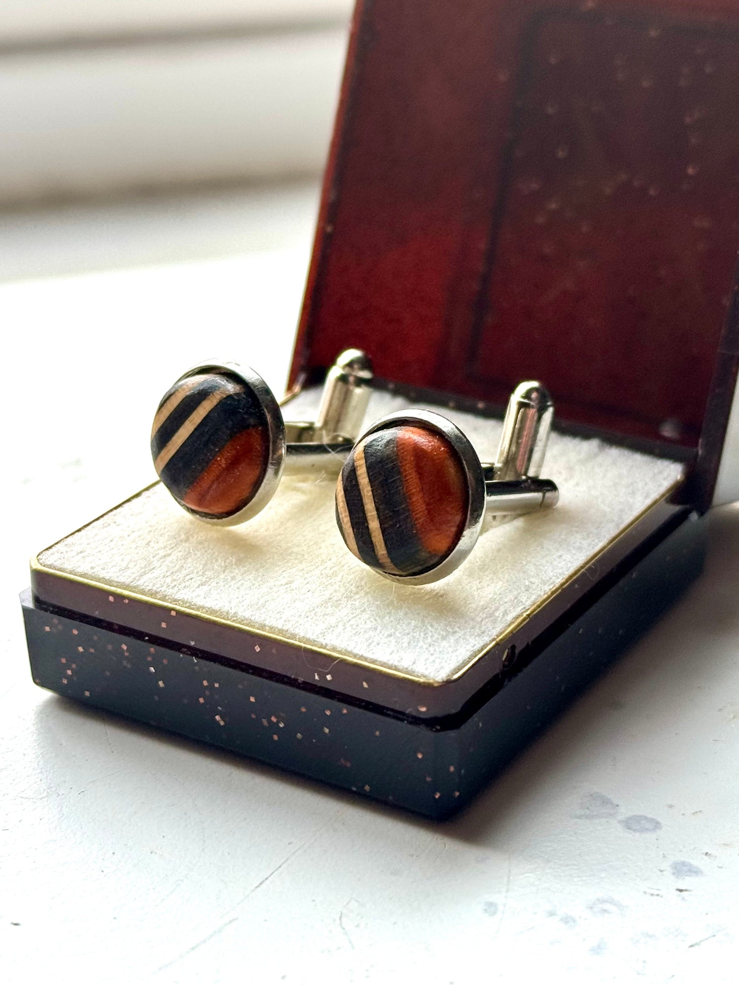 Handmade cufflinks with black and orange striped recycled skateboard wood inlays, set in silver-toned findings and displayed in a gift box