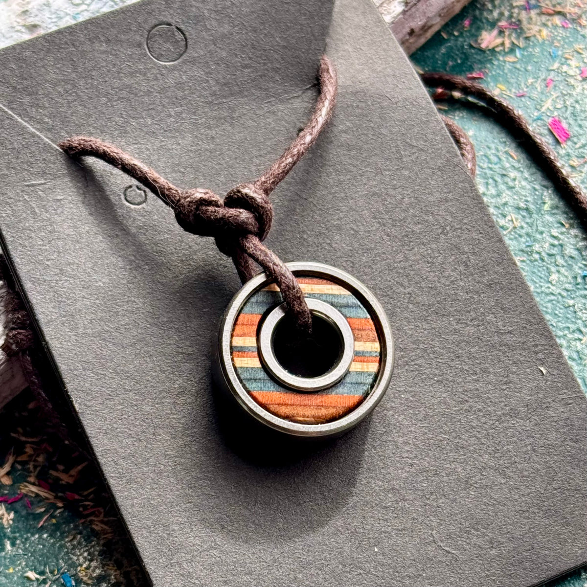 Orange and blue skateboard bearing pendant made from recycled skateboard maple on an adjustable cord.