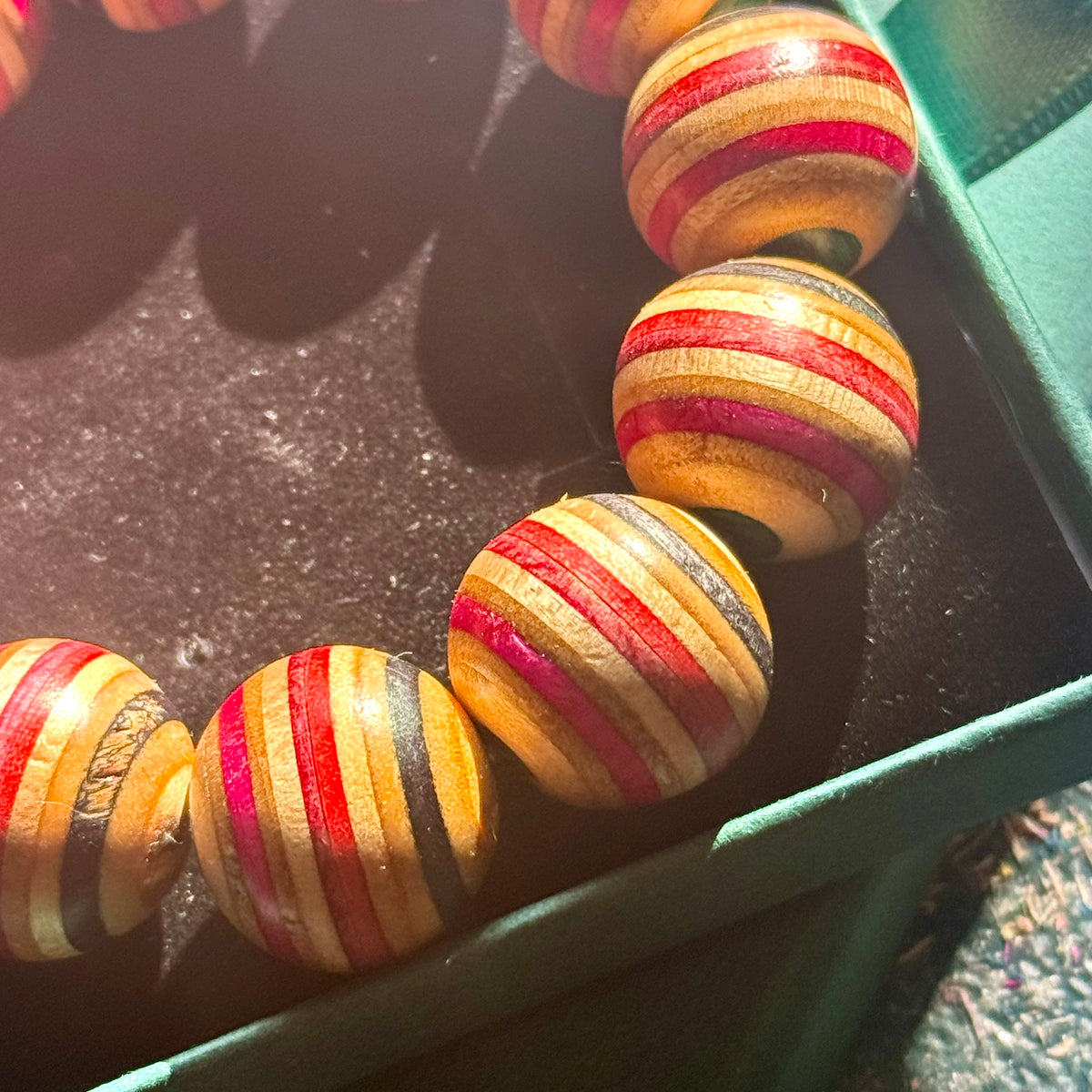 Large red, pink, black and teal beads cut from a recycled skateboard deck, resting at the edge of a gift box.