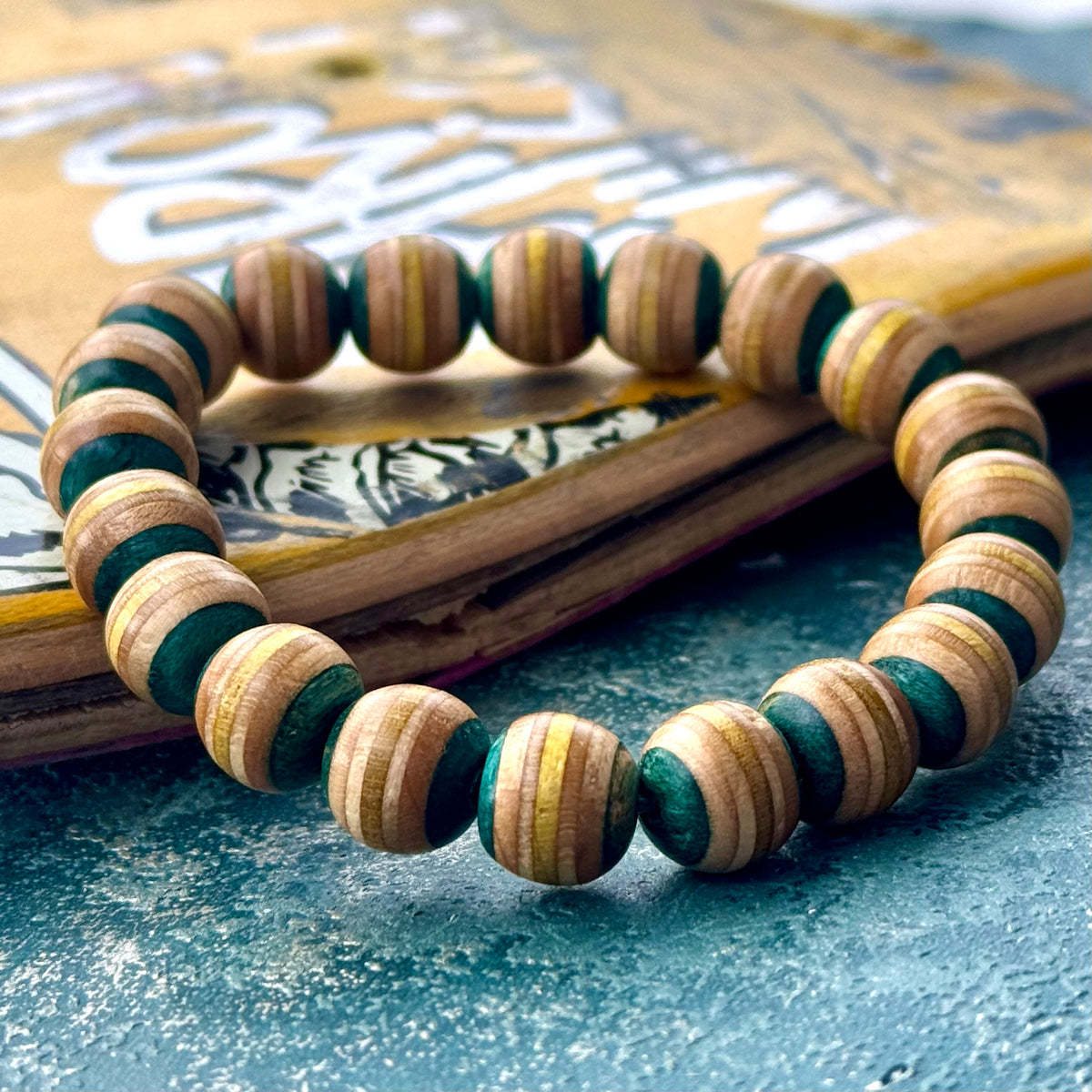 Wooden bead bracelet cut from a recycled skateboard deck, with light teal and yellow layers on every bead.