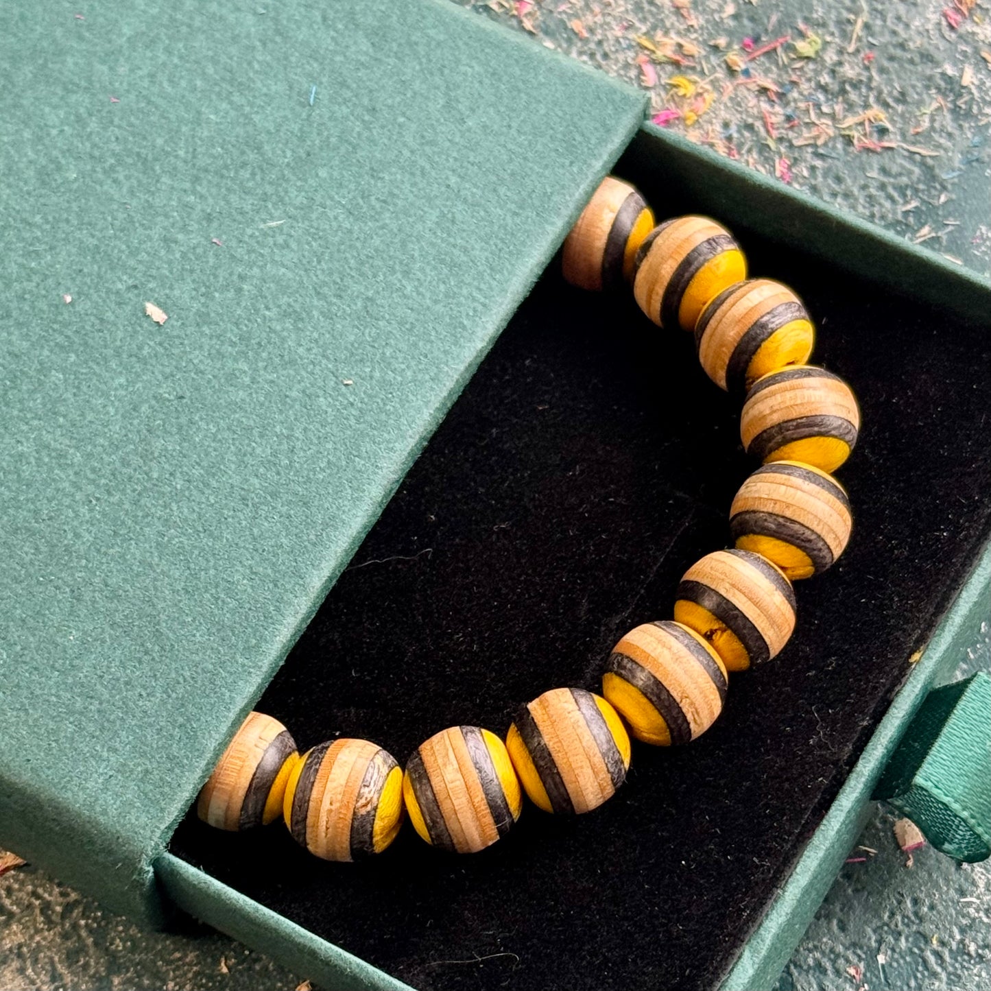 Yellow and black recycled skateboard wood bead bracelet in its gift box, photographed outdoors