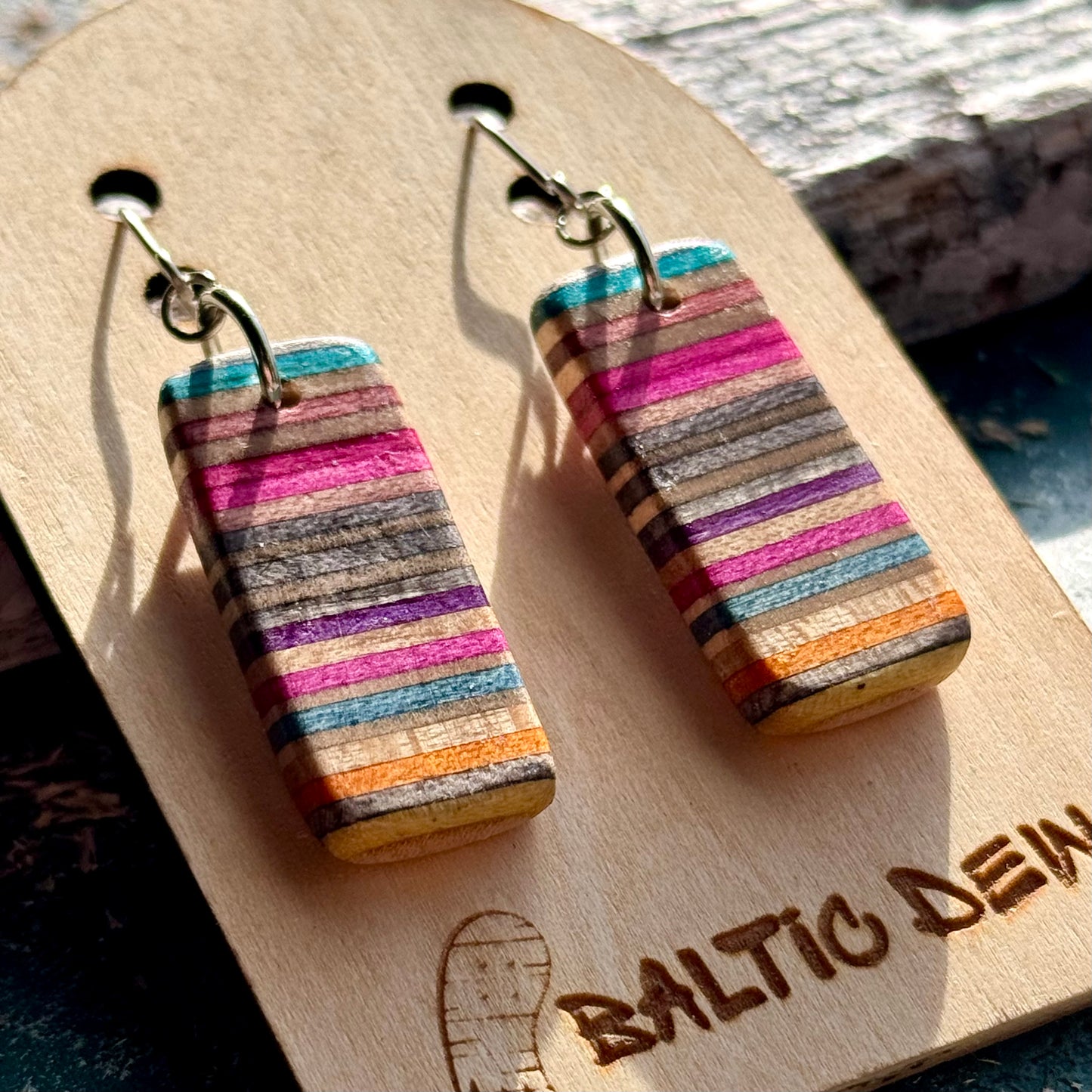 Multicoloured recycled skateboard wood drop earrings with the deck layers showing as stripes