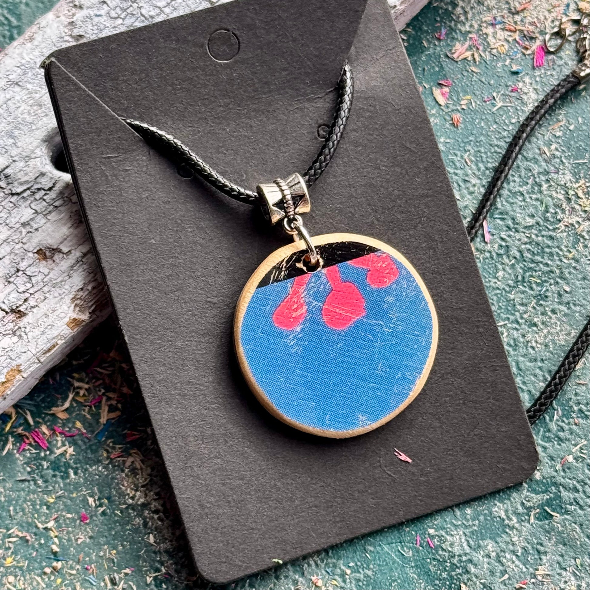 Recycled skateboard wood pendant with a blue face, pink flower detail and a natural maple rim.