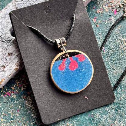 Recycled skateboard wood pendant with a blue face, pink flower detail and a natural maple rim.
