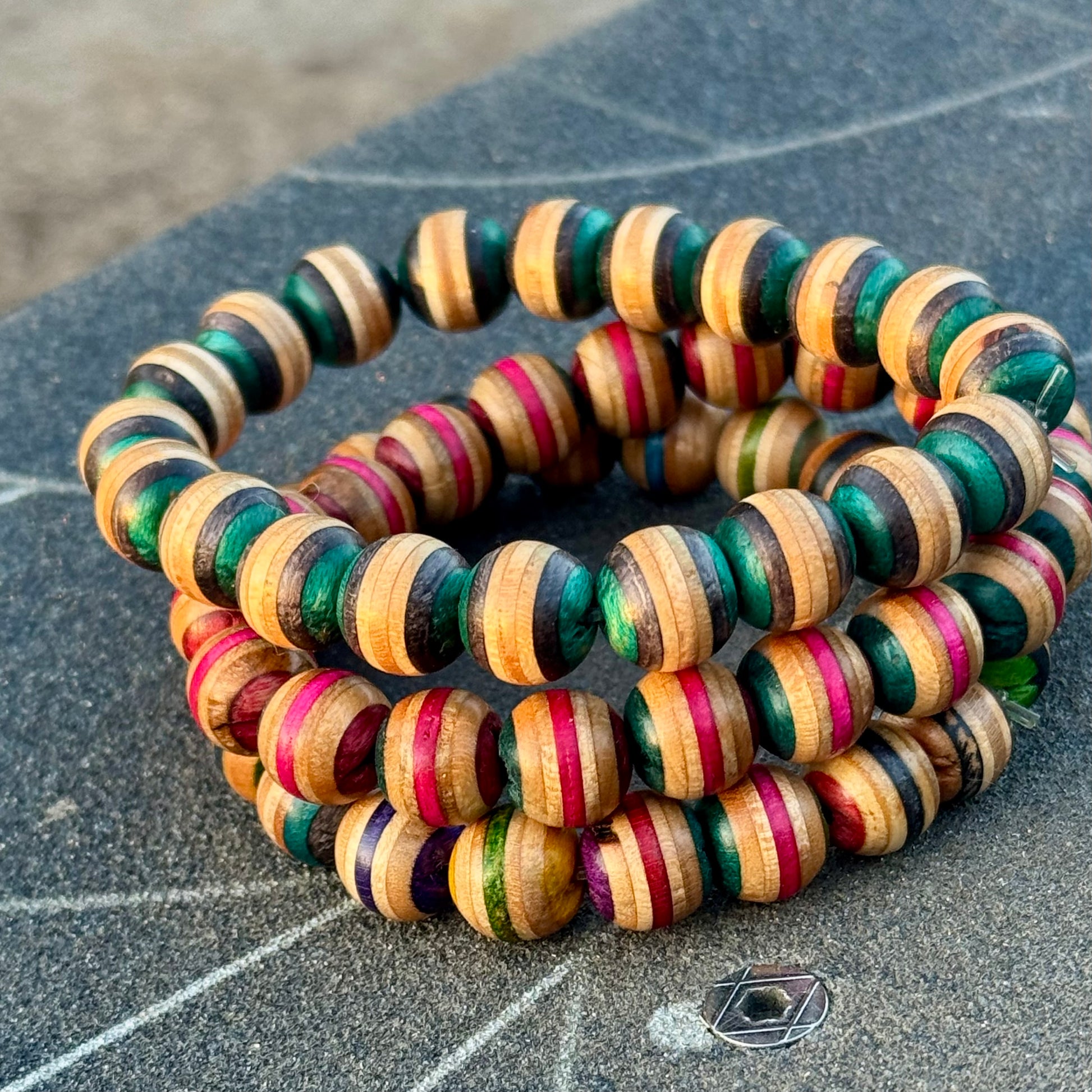 Recycled skateboard wood beaded bracelets stacked on a skatepark floor, showing the striped beads