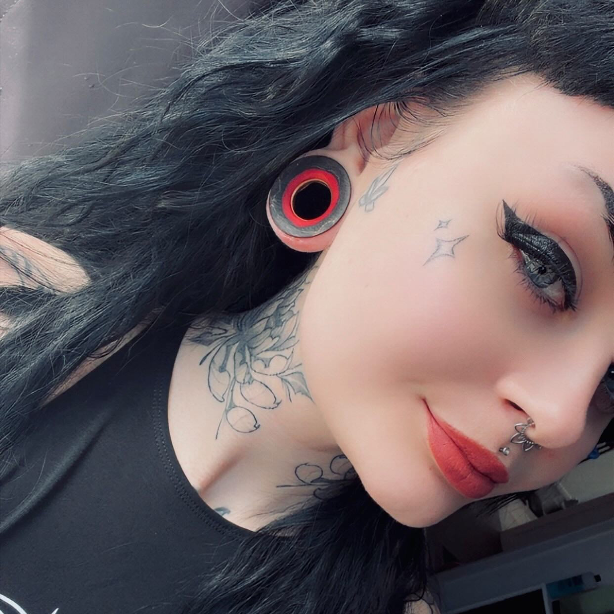 Red and black wooden flesh tunnel worn in a stretched lobe, seen close up from the side.