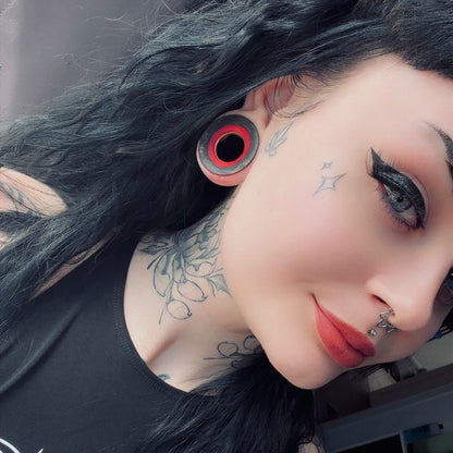 Red and black wooden flesh tunnel worn in a stretched lobe, seen close up from the side.