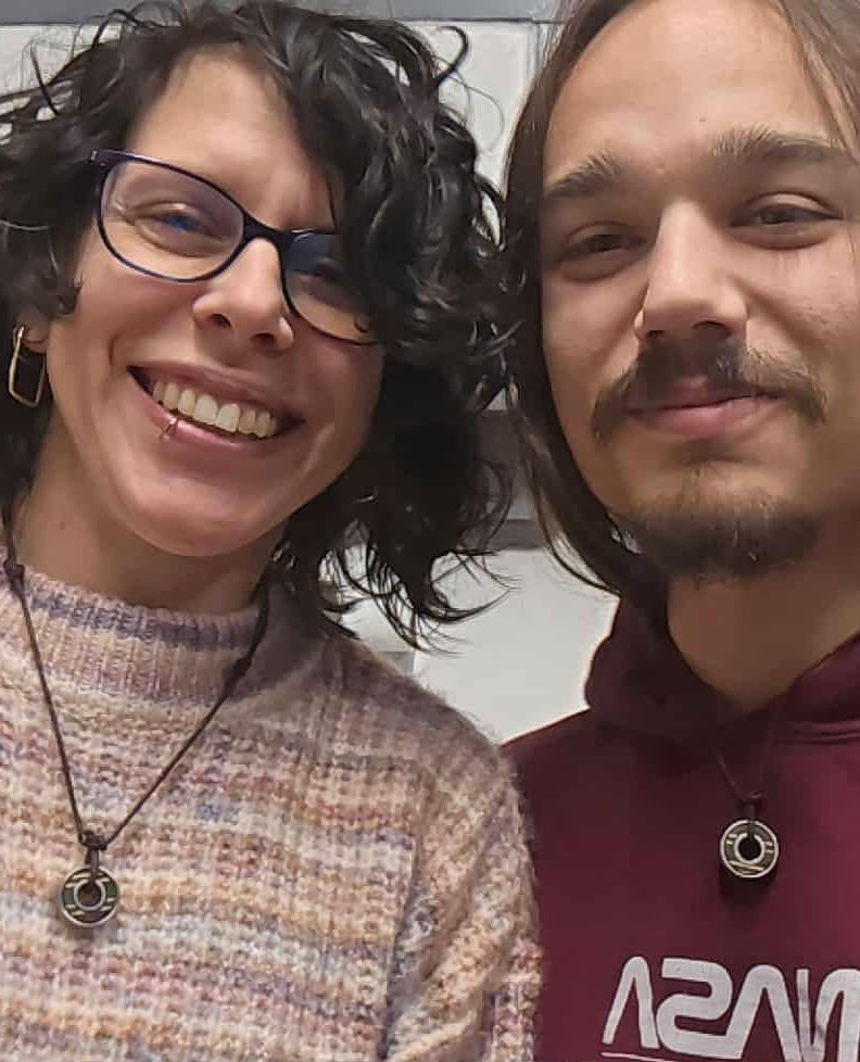 Two people each wearing a skateboard bearing pendant necklace