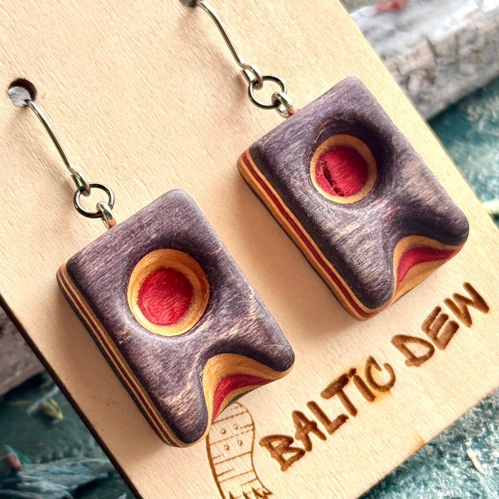 Close view of a purple wave earring with a red circle cut through the skateboard layers