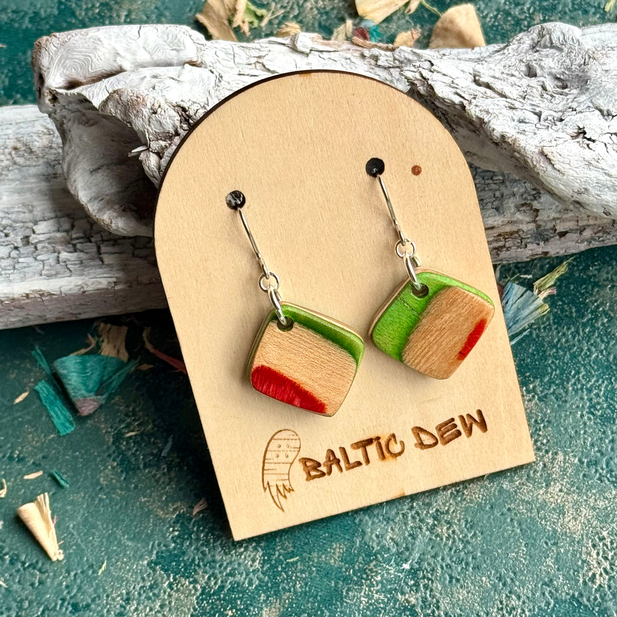 Small green and red square drop earrings with pale maple through the middle, cut from a skateboard deck