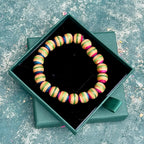Pink and green beaded bracelet made from recycled skateboard maple, shown from above in its green gift box.