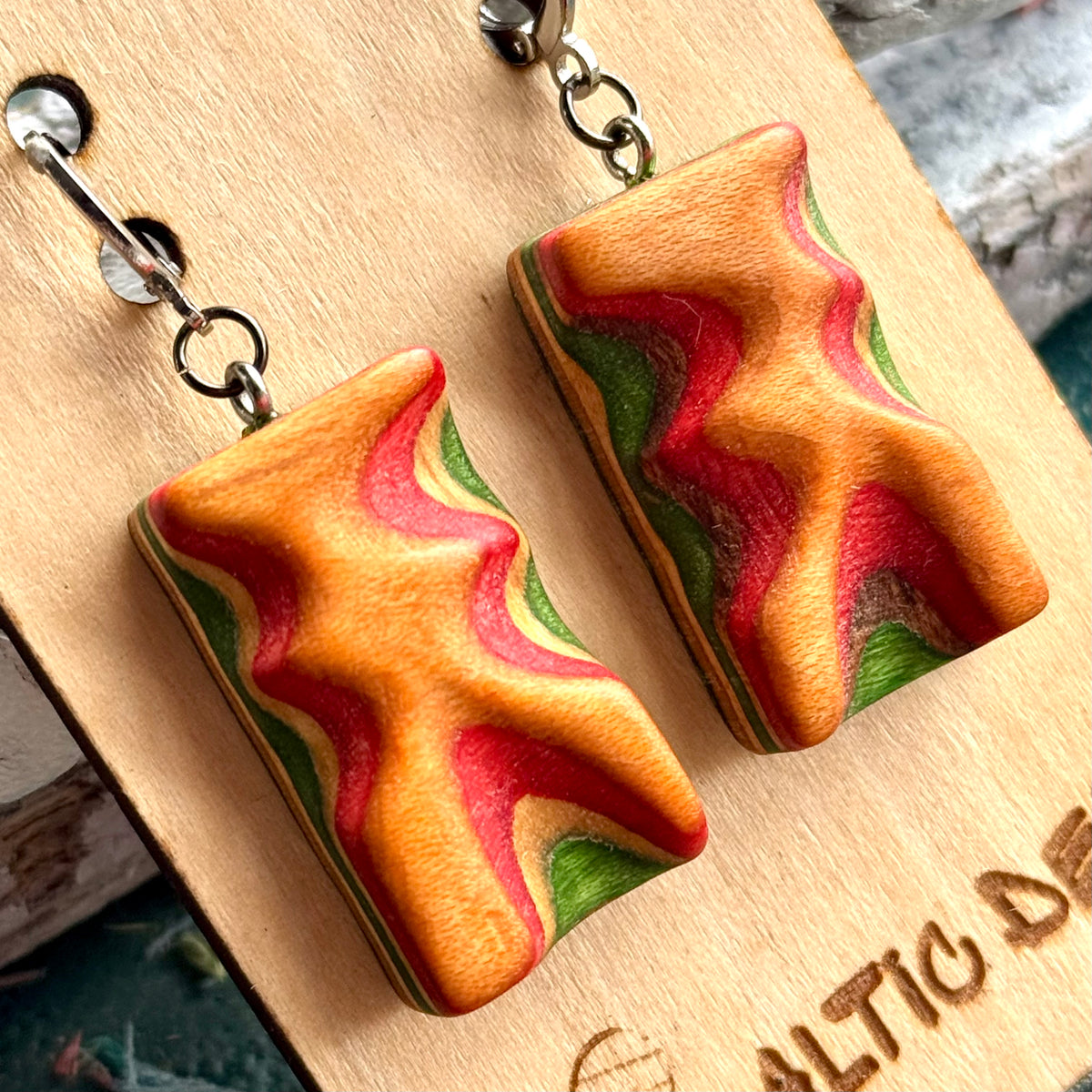 Close view of orange, red and green carved wave earrings cut from recycled skateboard maple