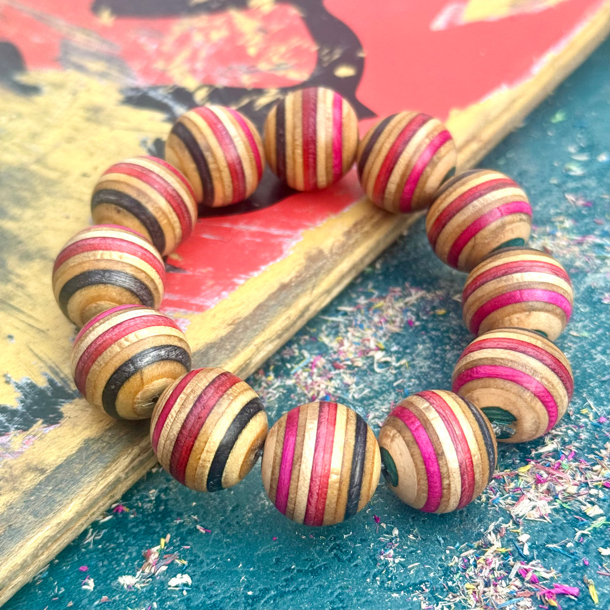 Chunky recycled skateboard wood bead bracelet in red, pink, black and teal on a red painted deck.