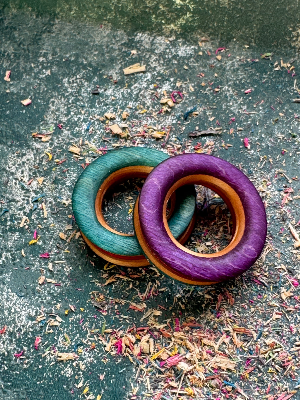Teal and purple skateboard wood tunnels with a warm maple bore, on a textured surface.
