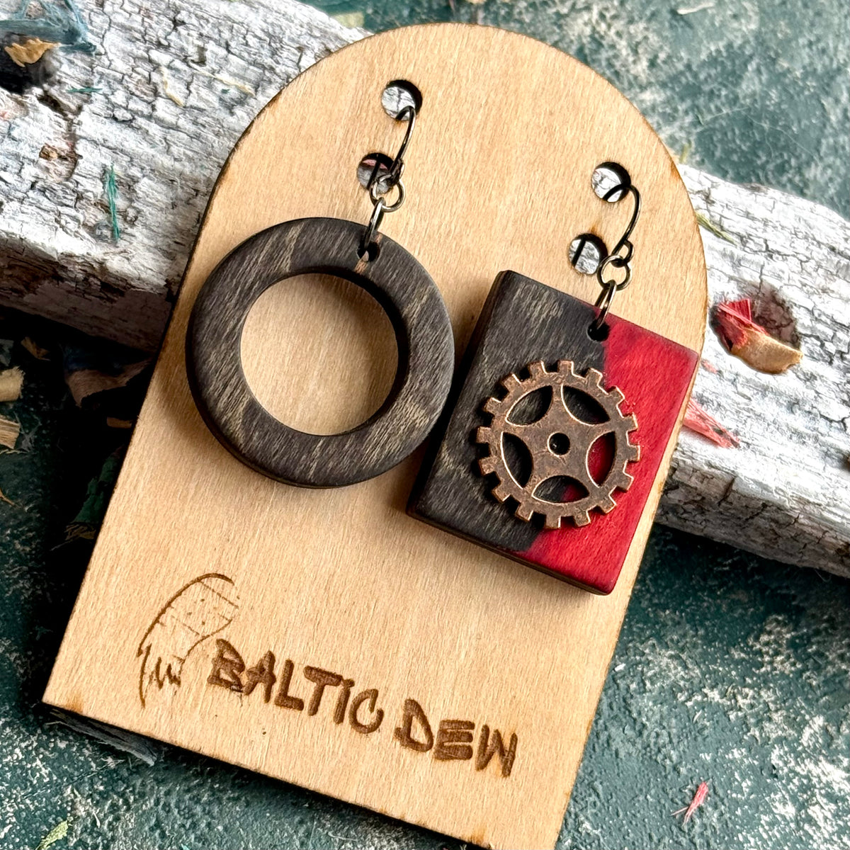 Mismatched skateboard wood earrings, a charcoal ring with a red square carrying a brass cog