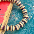 Close-up of purple, brown and black layers on beads cut from a recycled skateboard deck, handmade by Baltic Dew.