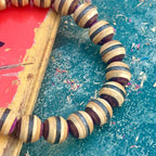 Close-up of purple, brown and black layers on beads cut from a recycled skateboard deck, handmade by Baltic Dew.