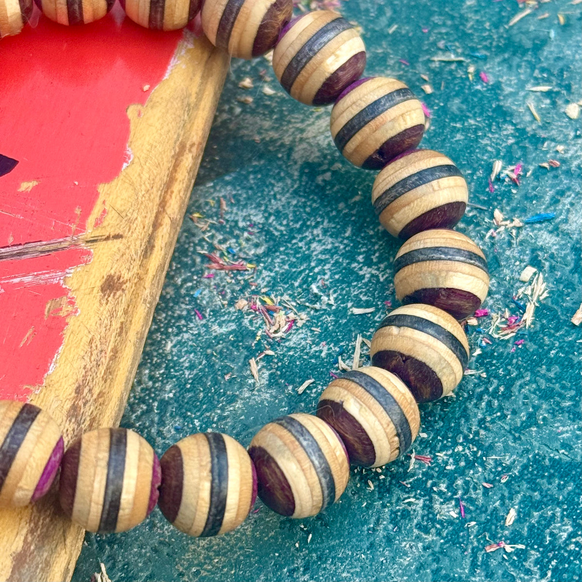 Close-up of purple, brown and black layers on beads cut from a recycled skateboard deck, handmade by Baltic Dew.