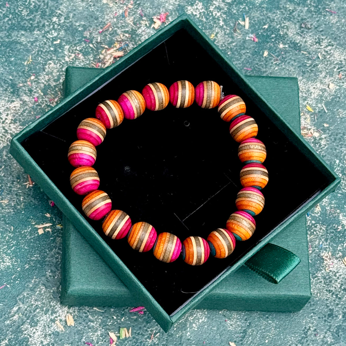 Orange and pink recycled skateboard wood bracelet shown from above in its green gift box, handmade by Baltic Dew.