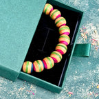 Recycled skateboard wood bracelet in pink and green, lying in an open gift box, handmade by Baltic Dew.