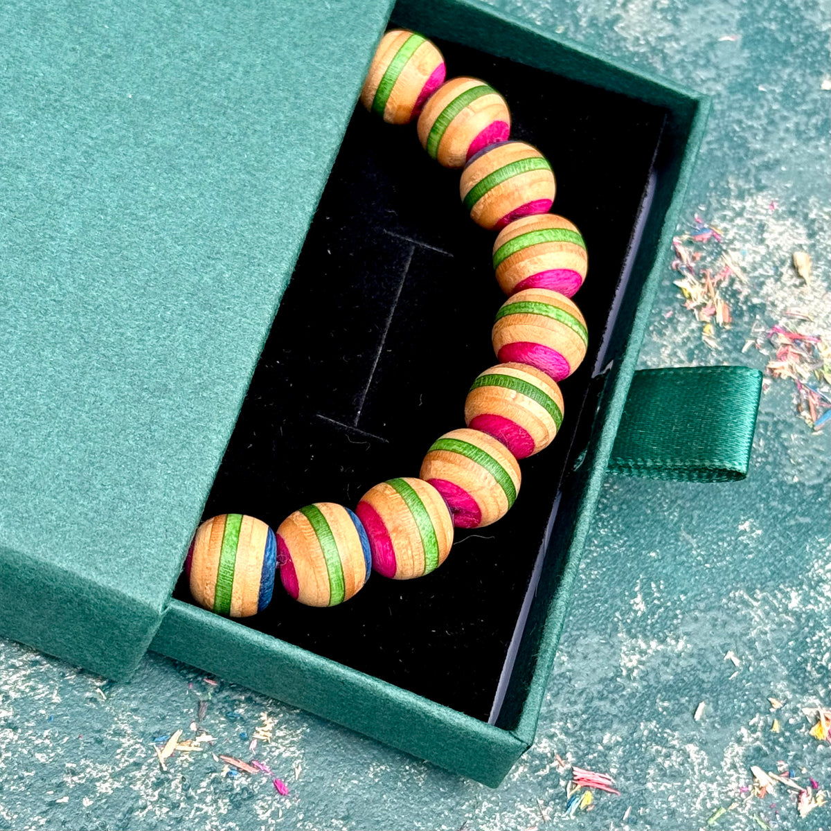 Recycled skateboard wood bracelet in pink and green, lying in an open gift box, handmade by Baltic Dew.