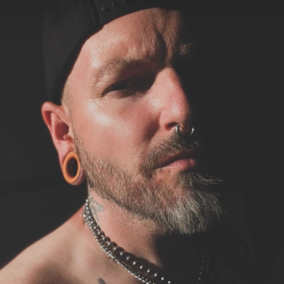 Orange wooden flesh tunnel worn in a stretched ear, photographed in low light.