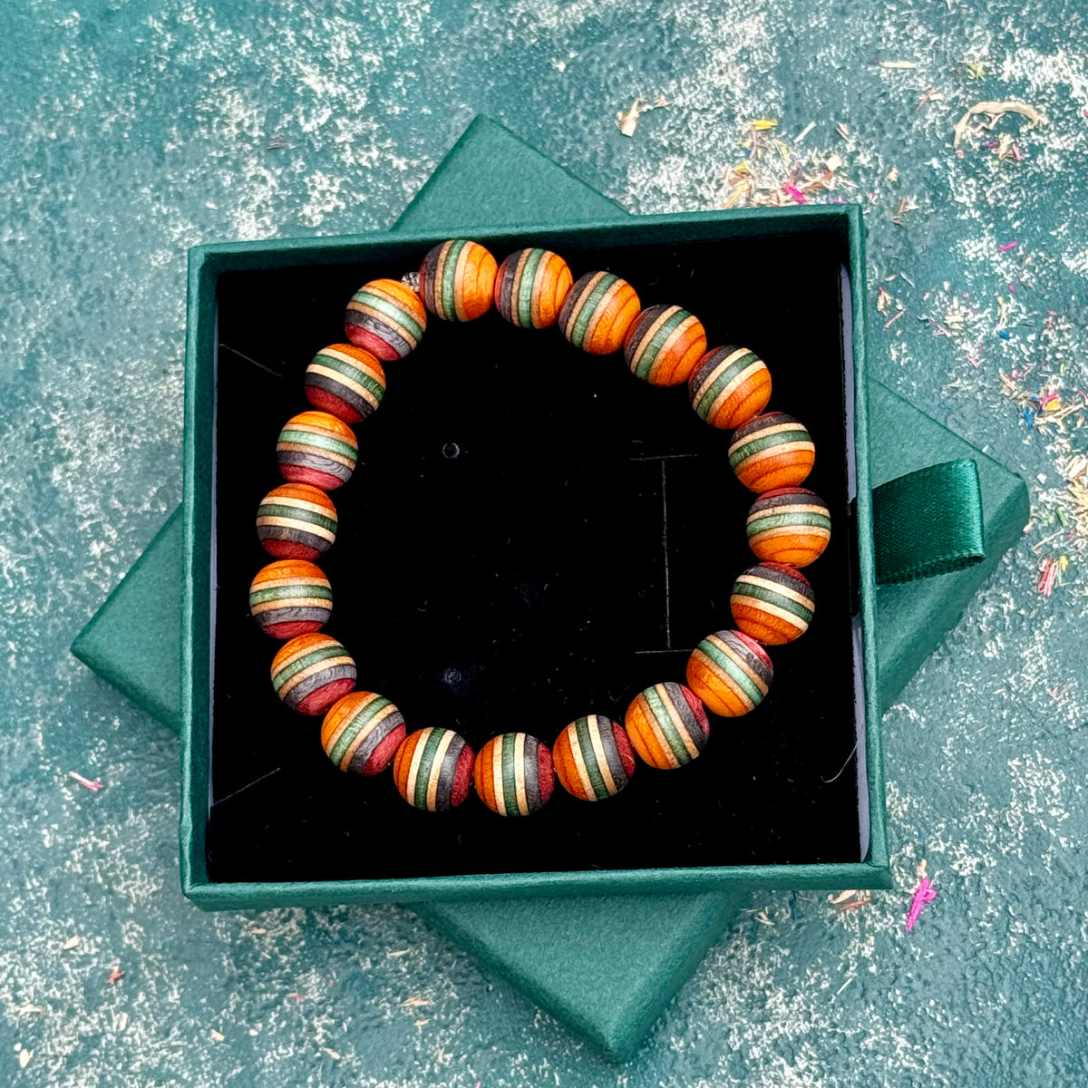 Orange, green and red wood bead bracelet from recycled skateboard maple, shown from above in its green gift box.