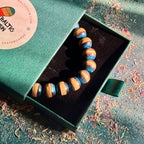 Blue and black recycled skateboard bracelet in its green Baltic Dew gift box, set on a dark surface.