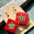 Red recycled skateboard square drop earrings with flower cut-outs displayed on a wooden Baltic Dew earring card.
