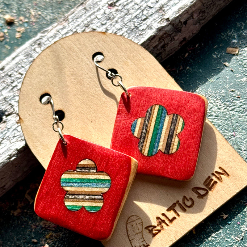 Red recycled skateboard square drop earrings with flower cut-outs displayed on a wooden Baltic Dew earring card.