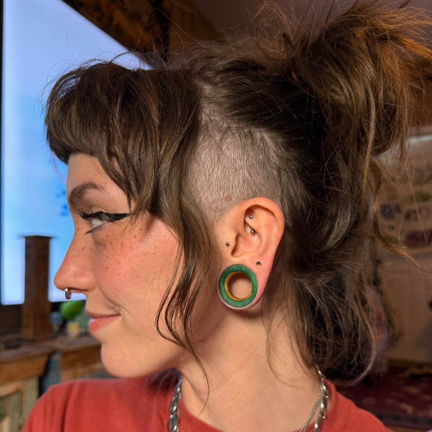 Green wooden ear tunnel worn in a stretched lobe, photographed outdoors in daylight.